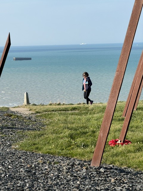Erin walking the clifftop at Arromanches with a Mulberry harbour caisson offshore
